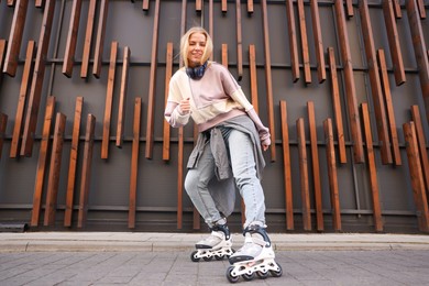 Photo of Beautiful young woman with roller skates near building outdoors, low angle view