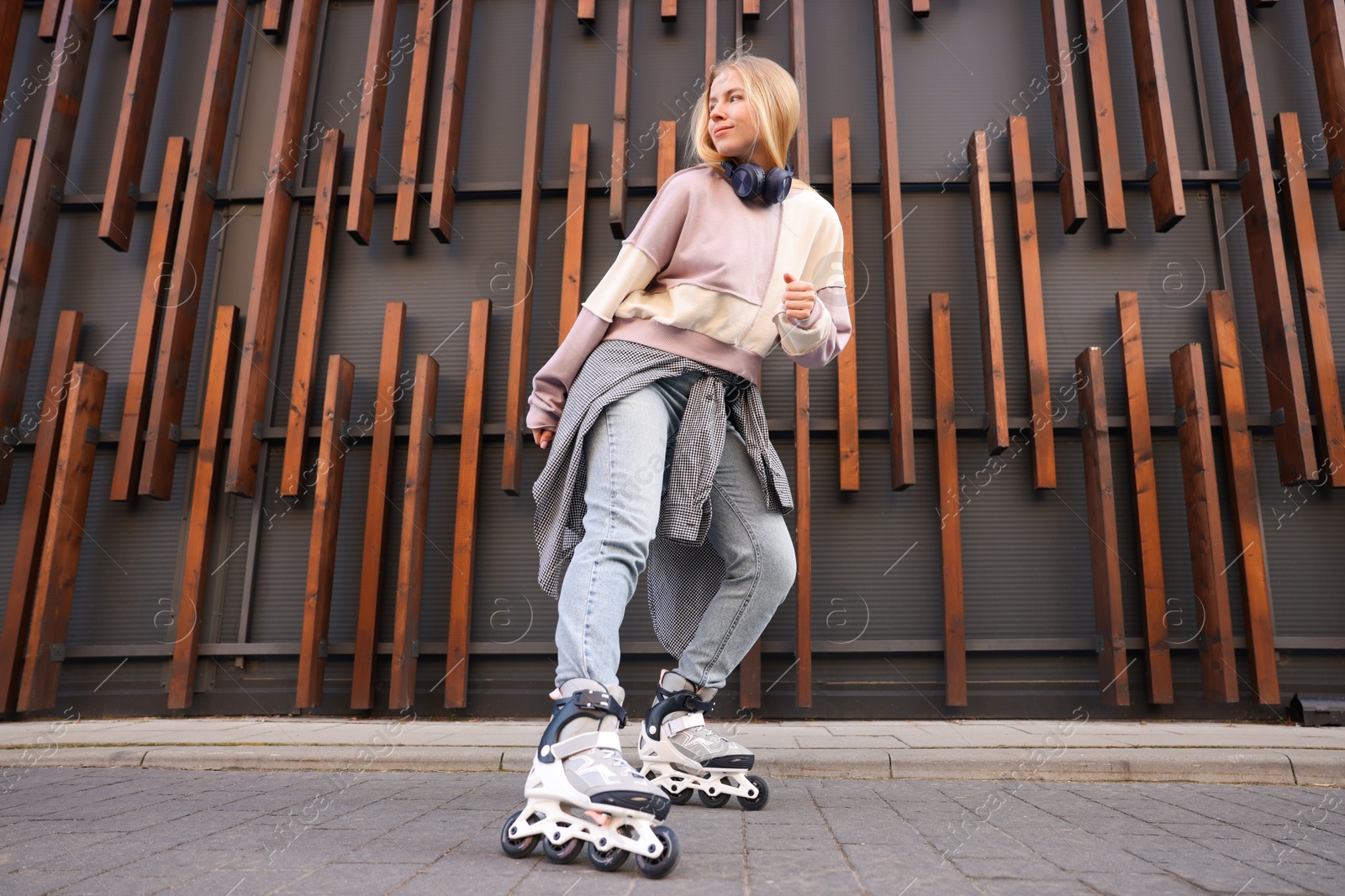 Photo of Beautiful young woman with roller skates near building outdoors, low angle view