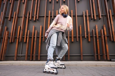 Photo of Beautiful young woman with roller skates near building outdoors, low angle view
