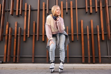 Photo of Beautiful young woman with roller skates near building outdoors, low angle view