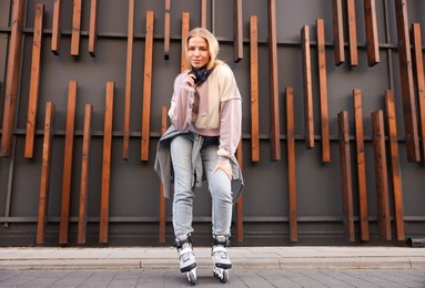 Photo of Beautiful young woman with roller skates near building outdoors, low angle view