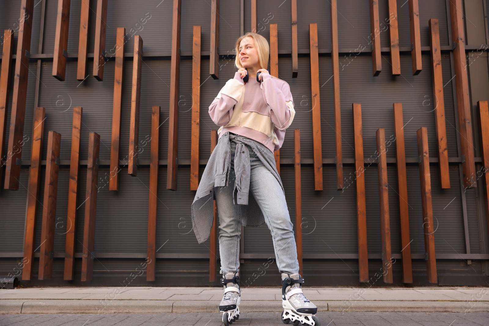 Photo of Beautiful young woman with roller skates near building outdoors, low angle view