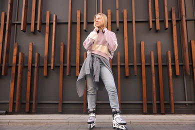 Photo of Beautiful young woman with roller skates near building outdoors, low angle view