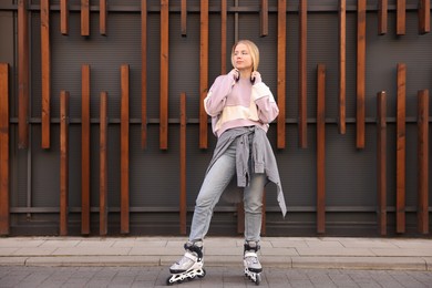 Photo of Beautiful young woman with roller skates near building outdoors