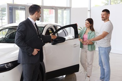Photo of Salesman with clipboard showing new car to happy family in salon