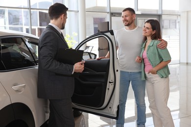 Photo of Salesman with clipboard showing new car to happy family in salon
