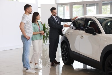 Photo of Salesman showing new car to happy family in salon