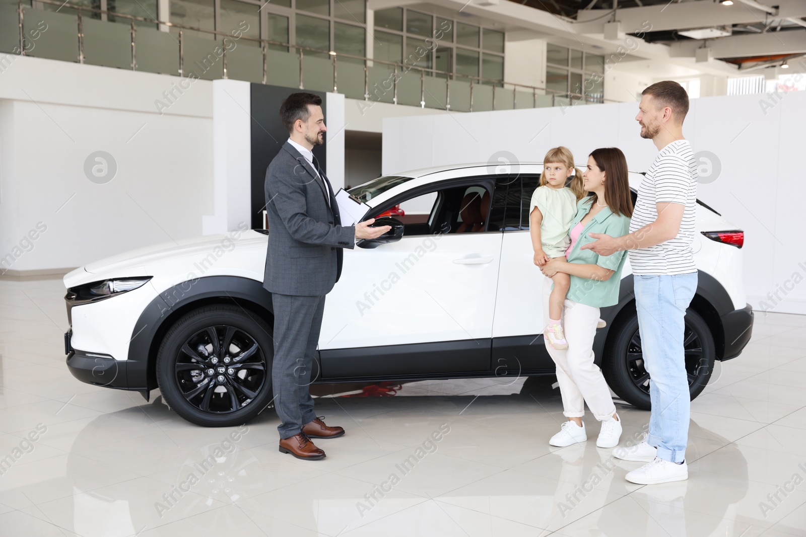 Smiling salesman with clipboard showing new car to family in salon Photo of Smiling salesman with clipboard showing new car to family in salon