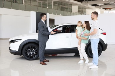 Photo of Smiling salesman with clipboard showing new car to family in salon