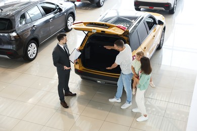 Photo of Salesman with clipboard showing new car to happy family in salon