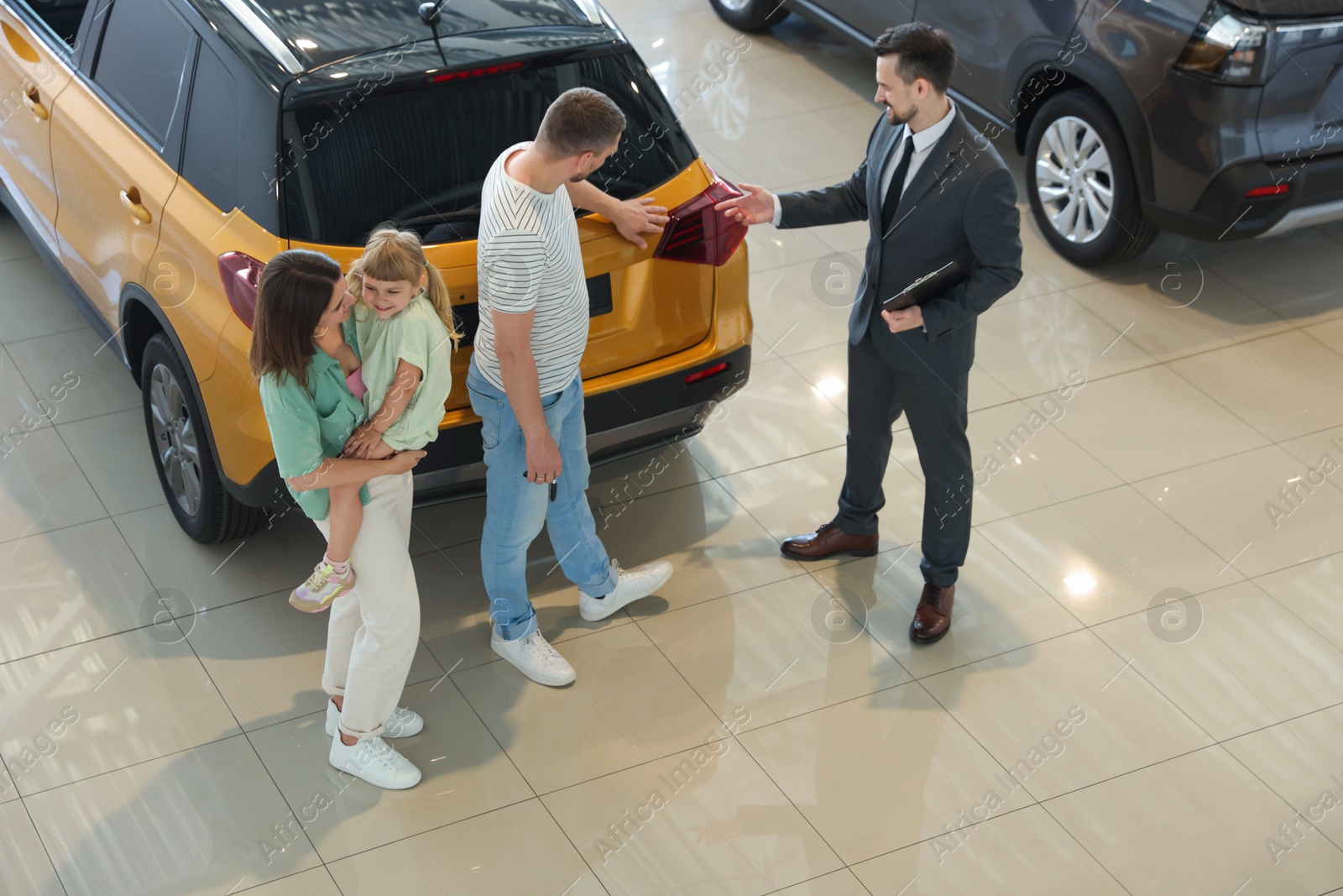 Photo of Salesman with clipboard showing new car to happy family in salon