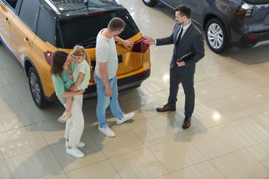 Photo of Salesman with clipboard showing new car to happy family in salon