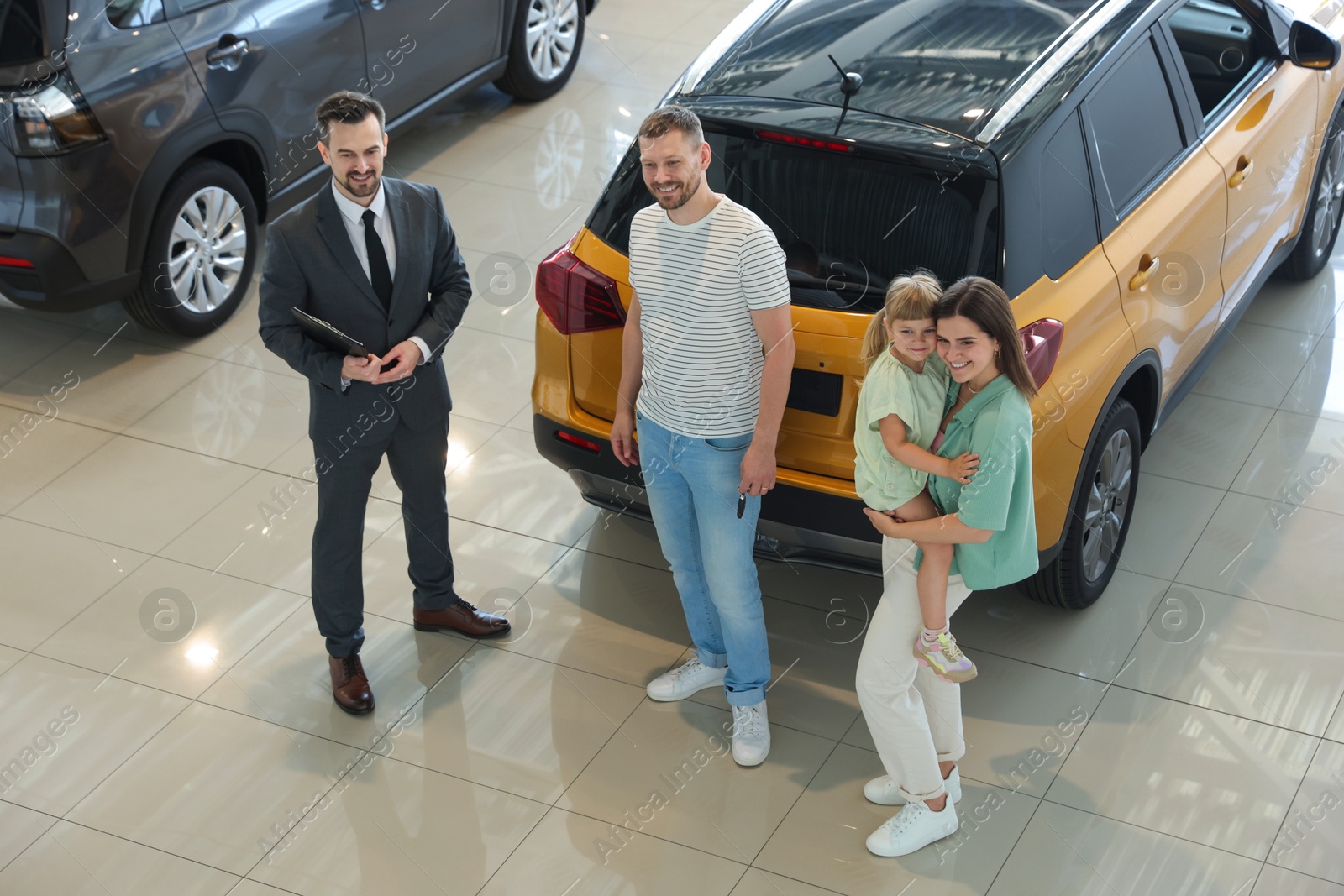 Photo of Salesman with clipboard showing new car to happy family in salon