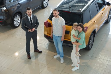 Photo of Salesman with clipboard showing new car to happy family in salon