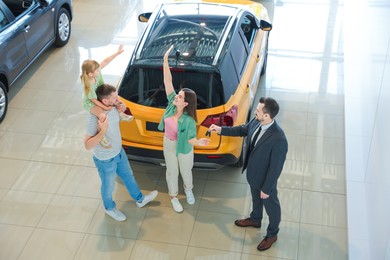 Photo of Salesman giving car key to happy family in salon