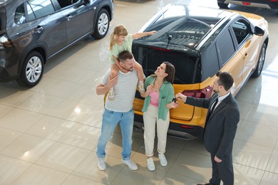 Photo of Salesman giving car key to happy family in salon