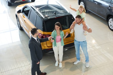 Photo of Salesman giving car key to happy family in salon