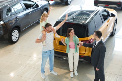 Photo of Salesman giving car key to happy family in salon