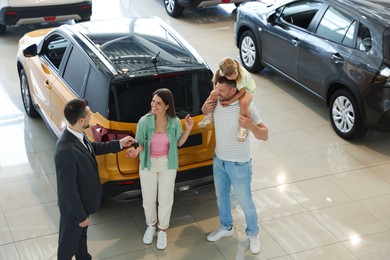 Photo of Salesman giving car key to happy family in salon