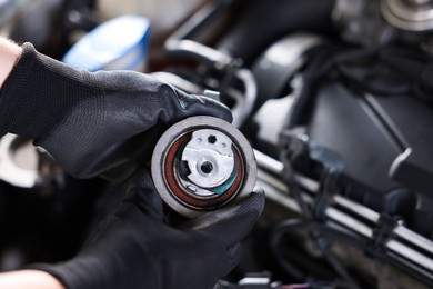 Photo of Auto part. Professional mechanic with idler-wheel near open hood of car indoors, closeup. Space for text