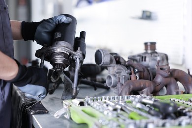 Photo of Auto parts. Professional mechanic with starter motor at table indoors, closeup