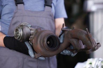 Photo of Auto part. Professional mechanic with turbocharger indoors, closeup