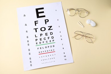 Photo of Vision test chart, glasses, tweezers and lenses on beige background, flat lay
