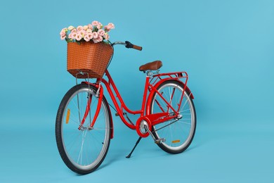 Photo of Bicycle with basket of beautiful flowers on light blue background