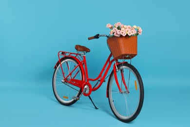 Photo of Bicycle with basket of beautiful flowers on light blue background
