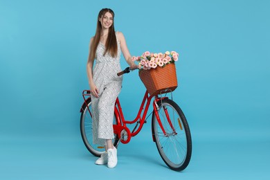 Photo of Smiling woman and bicycle with basket of flowers against light blue background