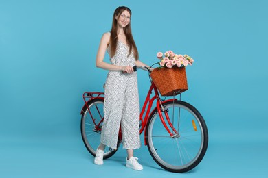 Photo of Smiling woman and bicycle with basket of flowers against light blue background