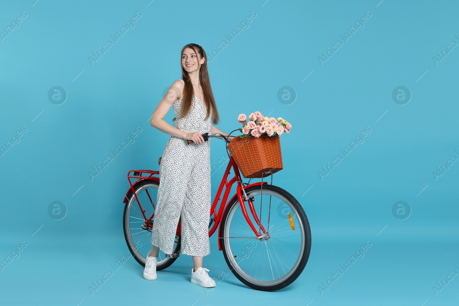 Photo of Smiling woman and bicycle with basket of flowers against light blue background