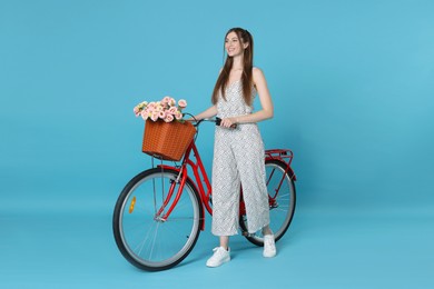 Photo of Smiling woman and bicycle with basket of flowers against light blue background