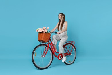 Photo of Smiling woman riding bicycle with basket of flowers against light blue background