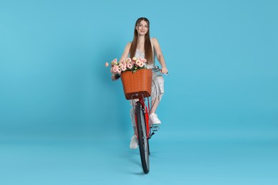 Photo of Beautiful woman riding bicycle with basket of flowers against light blue background