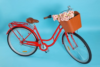 Photo of Bicycle with basket of beautiful flowers on light blue background