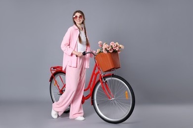 Photo of Smiling woman in sunglasses and bicycle with basket of flowers against grey background