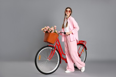 Photo of Smiling woman in sunglasses and bicycle with basket of flowers against grey background