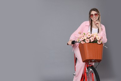 Photo of Smiling woman in sunglasses posing on bicycle with basket of flowers against grey background. Space for text