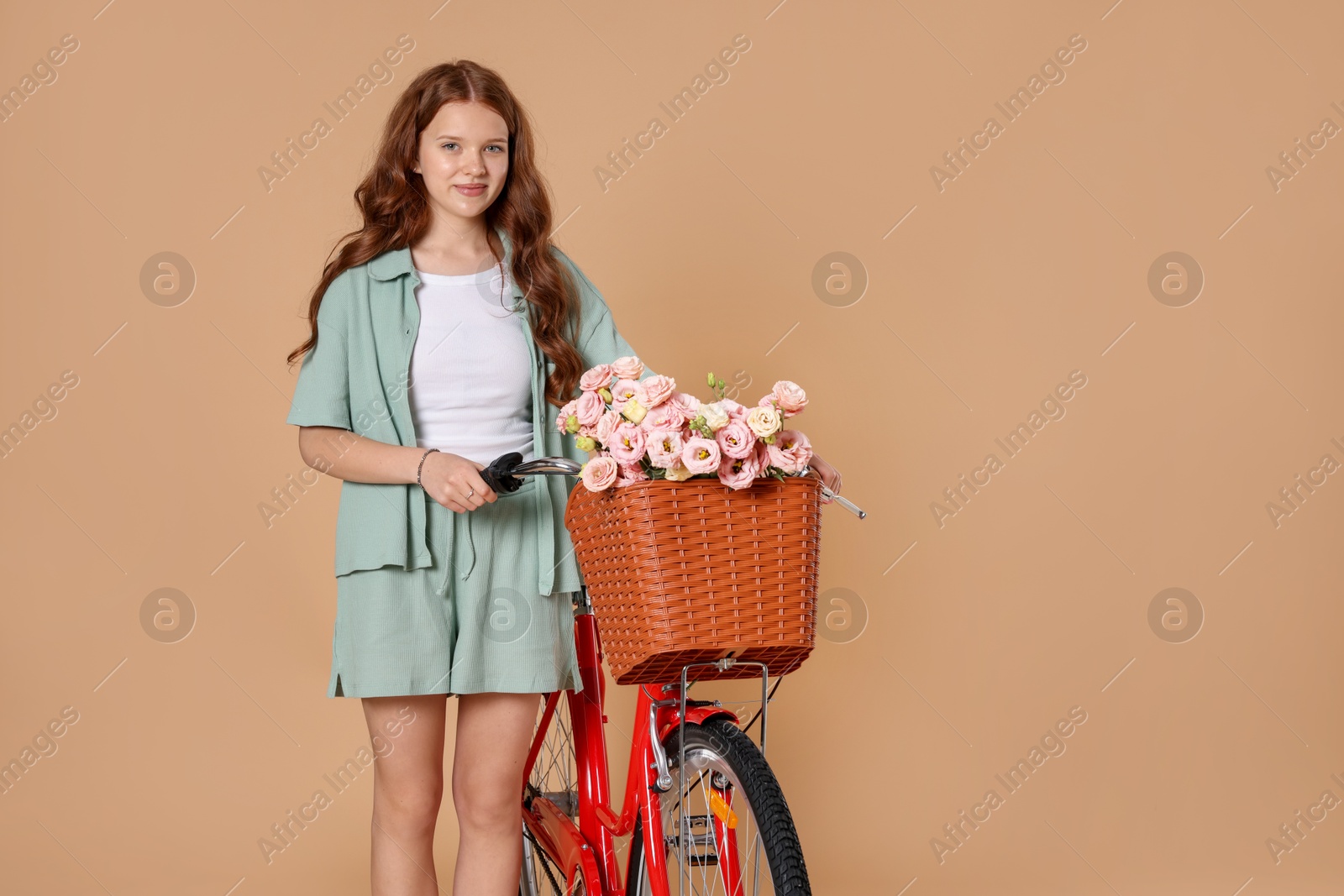 Beautiful teenage girl and bicycle with basket of flowers against beige background Photo of Beautiful teenage girl and bicycle with basket of flowers against beige background