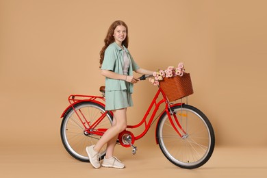 Photo of Smiling teenage girl and bicycle with basket of flowers against beige background
