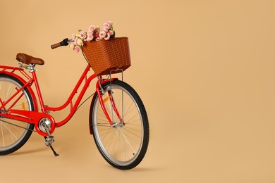 Photo of Bicycle with basket of beautiful flowers on pale orange background. Space for text