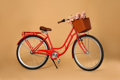 Photo of Bicycle with basket of beautiful flowers on pale orange background
