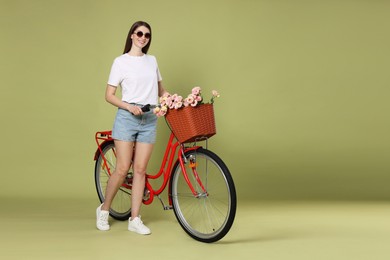 Photo of Smiling woman in sunglasses and bicycle with basket of flowers on green background. Space for text