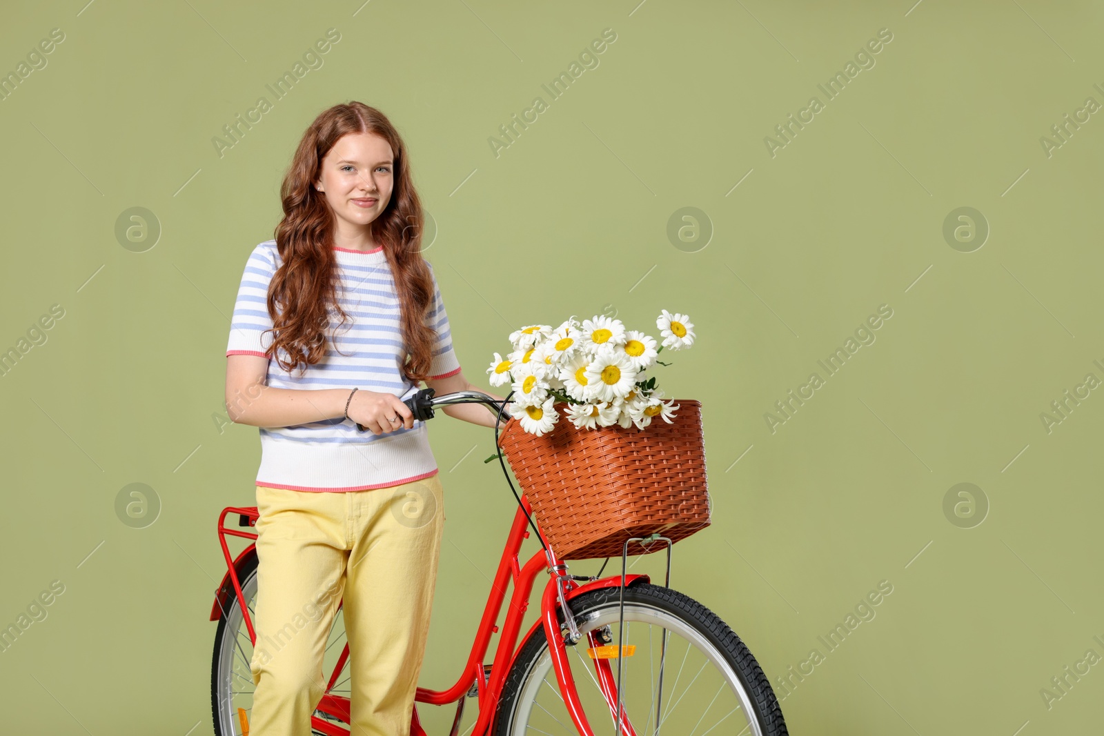 Photo of Beautiful teenage girl and bicycle with basket of flowers against green background. Space for text