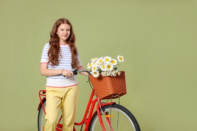 Photo of Beautiful teenage girl and bicycle with basket of flowers against green background. Space for text