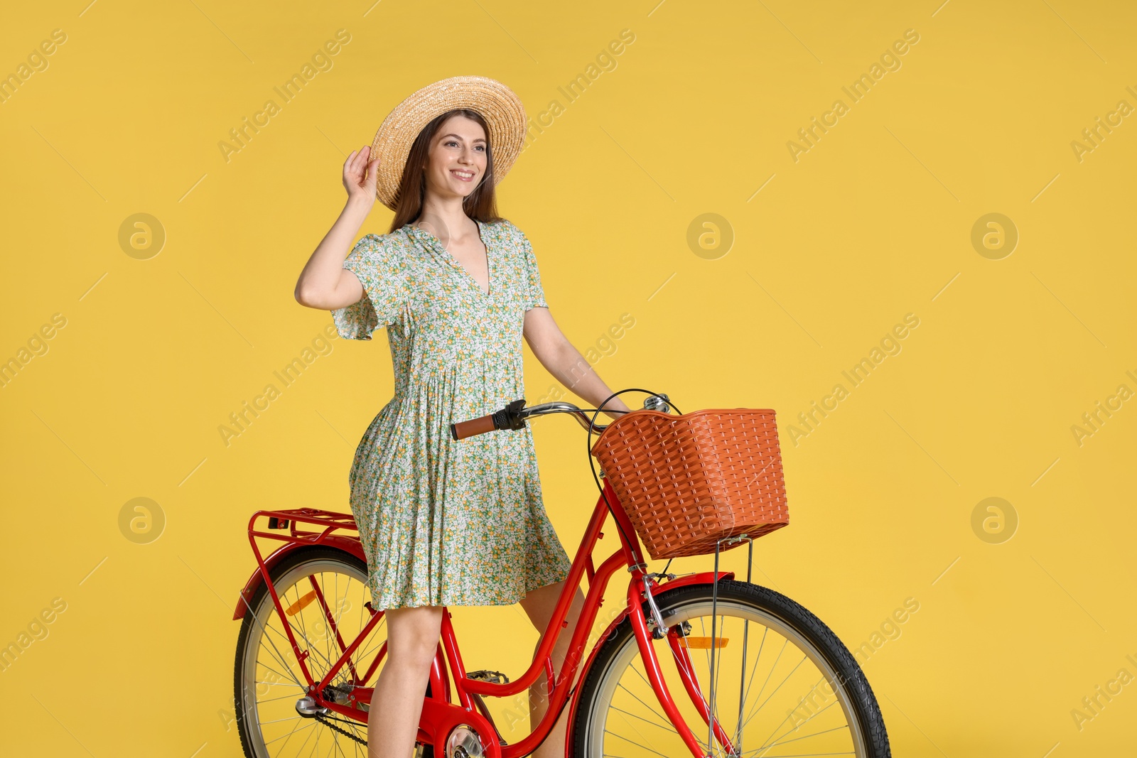 Photo of Smiling woman in hat riding bicycle with basket against yellow background