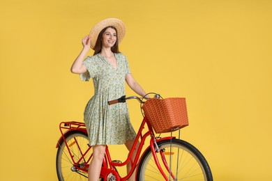 Photo of Smiling woman in hat riding bicycle with basket against yellow background