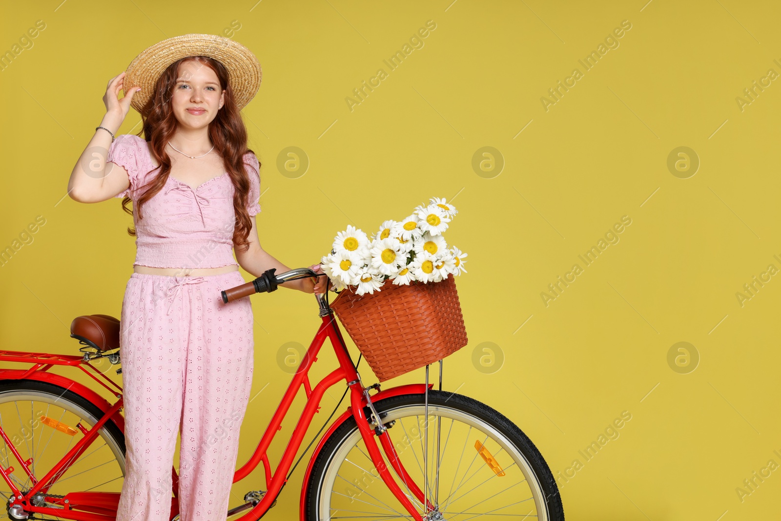 Beautiful teenage girl in hat and bicycle with basket of flowers against light green background. Space for text Photo of Beautiful teenage girl in hat and bicycle with basket of flowers against light green background. Space for text