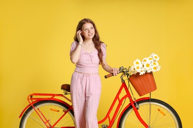 Photo of Smiling teenage girl and bicycle with basket of flowers against yellow background